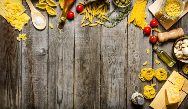 Pasta background. Several types of dry pasta with vegetables, cheese and herbs. — Stock Photo, Image