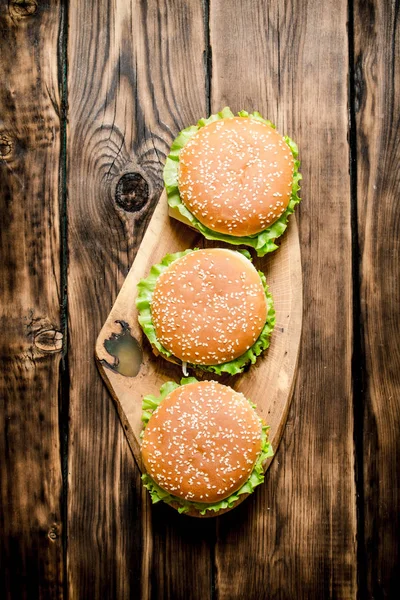 Three finished Burger with meat and vegetables on wooden stand.