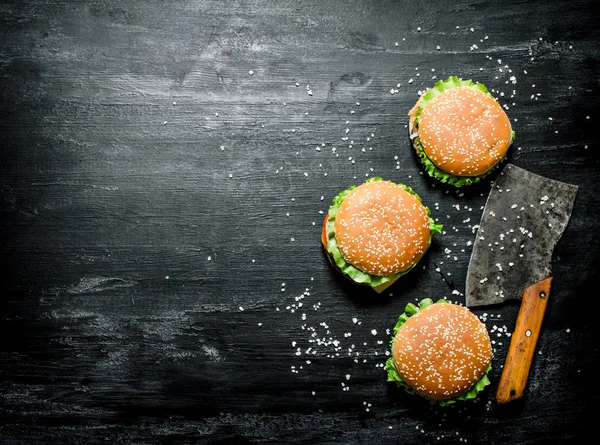 Three burgers with a meat ax. On black chalkboard.