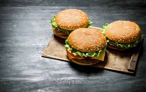 Tres hamburguesas en un tablero de madera . —  Fotos de Stock