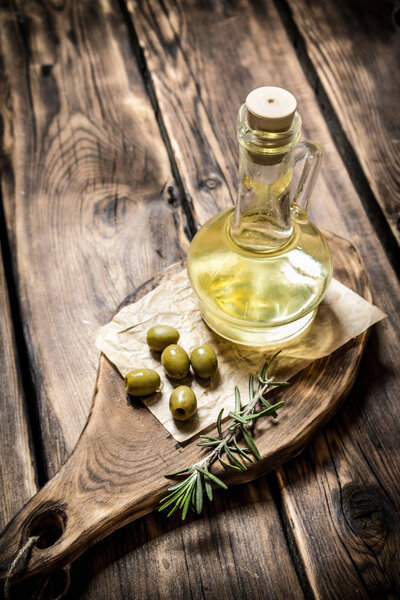 Olive oil with rosemary branch. On wooden background.