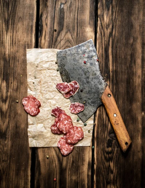 Salame fatiado e um machado velho. Em fundo de madeira . — Fotografia de Stock