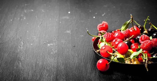 Wild berries in the old plate. On black wooden background. — Stock Photo, Image