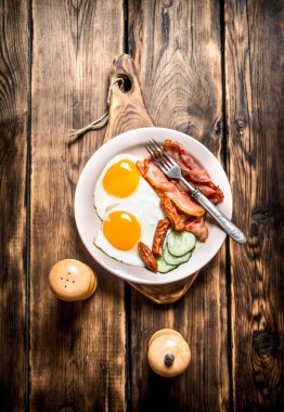 tabak kızarmış yumurta, pastırma, salatalık ve tütsülenmiş sosis.