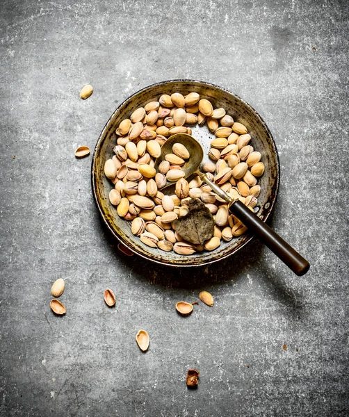 Bir kepçe ile eski bir tavada Antep fıstığı.