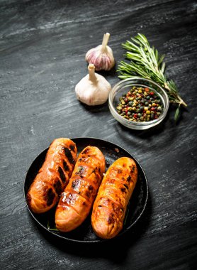 Sarımsak ve otlar bir tavada kızarmış sosis. 