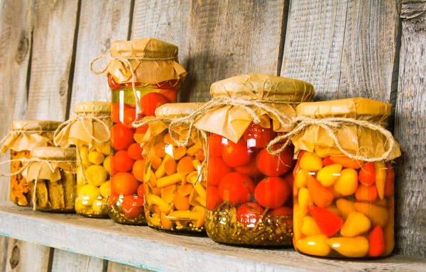Preserved food in glass jars, on a wooden shelf. — Stock Photo, Image