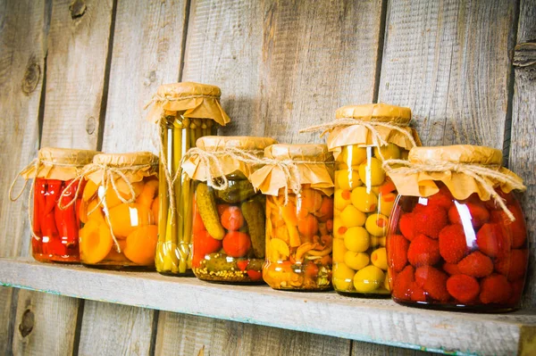 Preserved food in glass jars, on a wooden shelf. — Stock Photo, Image