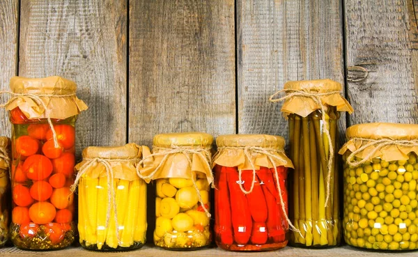 Preserved food in glass jars, on a wooden shelf.