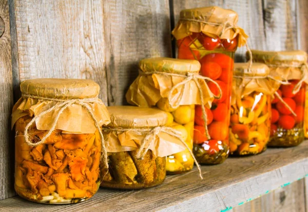 Preserved food in glass jars, on a wooden shelf. — Stock Photo, Image