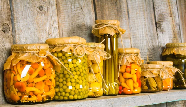 Preserved food in glass jars, on a wooden shelf. — Stock Photo, Image