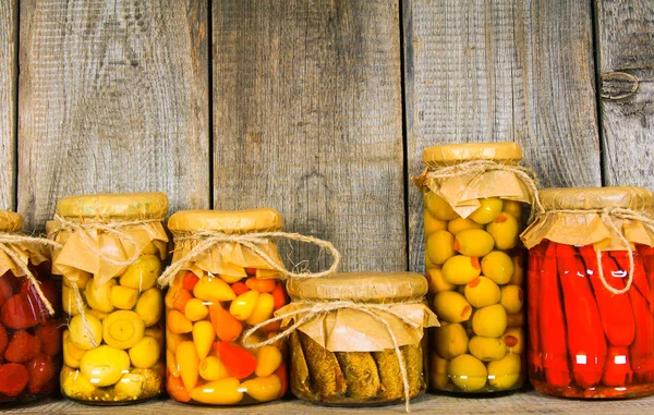 Preserved food in glass jars, on a wooden shelf. — Stock Photo, Image