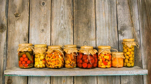 Preserved food in glass jars, on a wooden shelf. — Stock Photo, Image