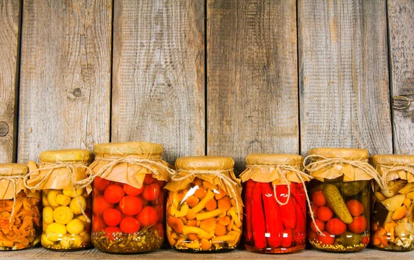 Preserved food in glass jars, on a wooden shelf. — Stock Photo, Image