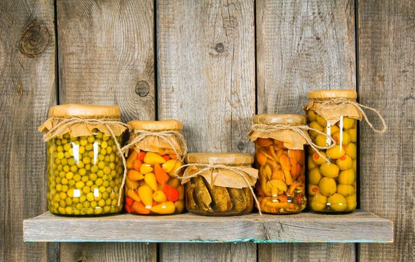 Preserved food in glass jars, on a wooden shelf.