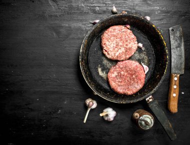 Eski bir tavada sarımsak ve baharat ile sığır gelen ham burger.
