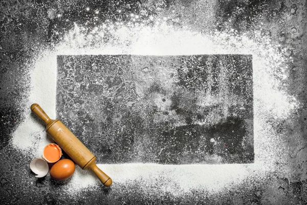 Baking background. A frame of flour with a rolling pin and fresh eggs.