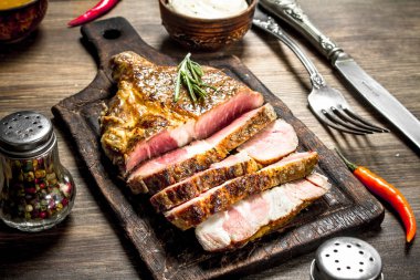 Bir kesme tahtası üzerinde baharatlar ile sığır eti ızgara. Ahşap bir masaya.