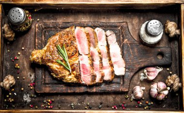 Bir kesme tahtası üzerinde baharatlar ile sığır eti ızgara. Ahşap bir masaya.