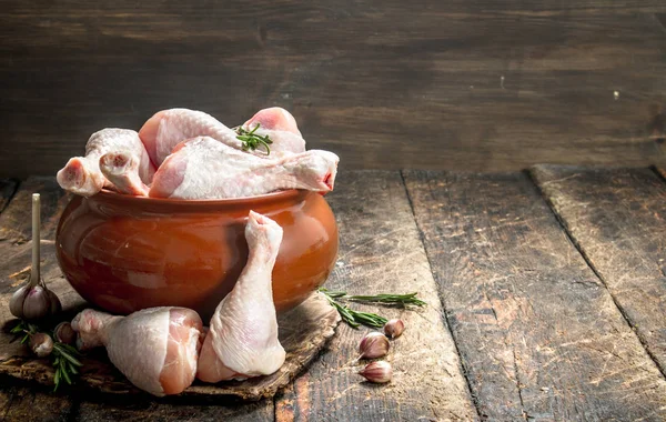 Raw chicken legs with garlic and spices in a bowl. On wooden background.