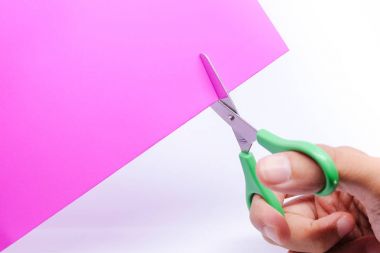 Beyaz arka plan üzerinde izole mor kağıt kesim için kullanılan yeşil makas tutan el.
