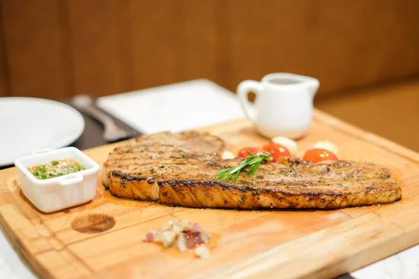 Izgara domuz tomahawk (domuz pirzolası) demirhindi sos, kara biber sosu, domates, sarımsak ve tuz ile hizmet ahşap plaka üzerinde.