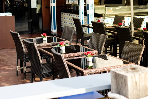 Molte sedie in rattan nero con rosa rossa in vaso e tavolo chiaro impostato sul pavimento in legno al ristorante per lo sfondo cibo di strada o consistenza concetto esterno . — Foto Stock