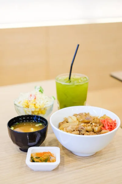 O conjunto de alimentos consiste em arroz com carne de porco grelhada teriyaki, cebolinha e cenoura no topo tigela branca servir com sopa de tofu (sopa Miso), tomate, repolho e salada de milho e chá verde conceito de comida japonesa . — Fotografia de Stock