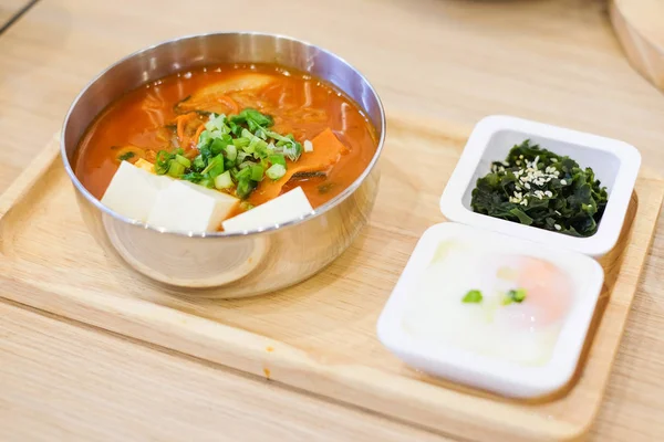 Hemlagad mat består av kryddig kimchi-soppa (bacon, bit fläsk, vit tofu, vårlök & kål), mjuka kokt ägg (onsen), gröna alger med vit sesam tjäna på träbricka. — Stockfoto