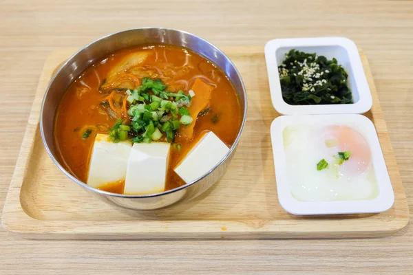 Hemlagad mat består av kryddig kimchi-soppa (bacon, bit fläsk, vit tofu, vårlök & kål), mjuka kokt ägg (onsen), gröna alger med vit sesam tjäna på träbricka. — Stockfoto