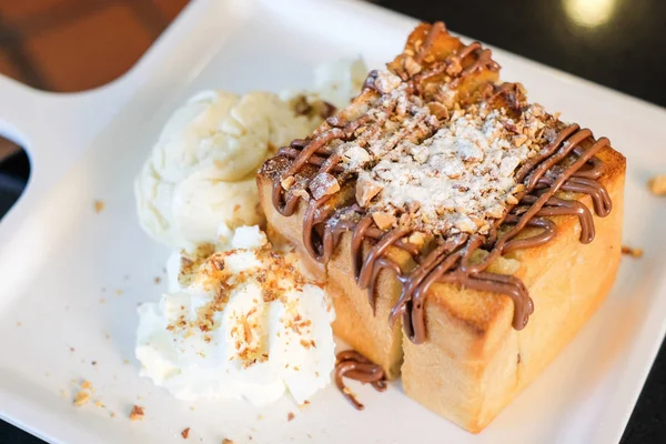 El pan tostado rematado con chocolate y almendras, crema batida y helado de vainilla sirven en plato blanco para fondo de postre o textura . — Foto de Stock