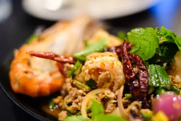 Big shrimps and squids and spicy minced pork mixed together with various herbs and vegetables including dried chilli served on black plate, for thai food background or texture. — Stock Photo, Image