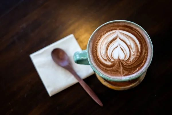 Secangkir cokelat panas (kopi atau latte) yang dihias dengan susu hati di permukaan yang diletakkan di atas nampan kayu dan sendok yang diletakkan di atas jaringan, untuk minuman / minuman latar belakang atau tekstur - konsep diet sehat . — Stok Foto