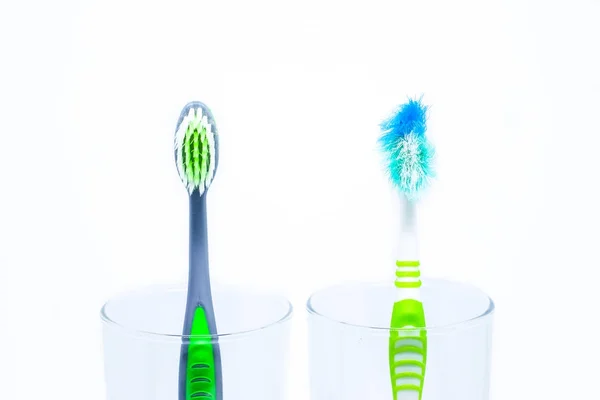 New toothbrush and old toothbrush (damaged) in clear glass for teeth cleaning isolated on white background - concept " How often should you change your toothbrush ? " — Stock Photo, Image