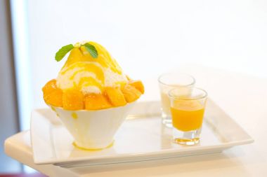 Mango kakigori (Japon kesilmiş buz tatlı lezzet mango dondurma ile) hizmet üzerinde sarı mango sos ve beyaz süt tatlı gıda arka plan veya doku ile beyaz kase.