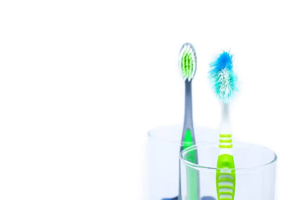 New toothbrush and old toothbrush (damaged) in clear glass for teeth cleaning isolated on white background - concept "How often should you change your toothbrush ? " — Stock Photo, Image
