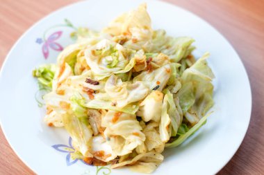 Yakın plan kızarmış lahana ve balık sosu kahverengi masadaki beyaz tabakta servis edilir. Ev yapımı yiyecek konsepti..