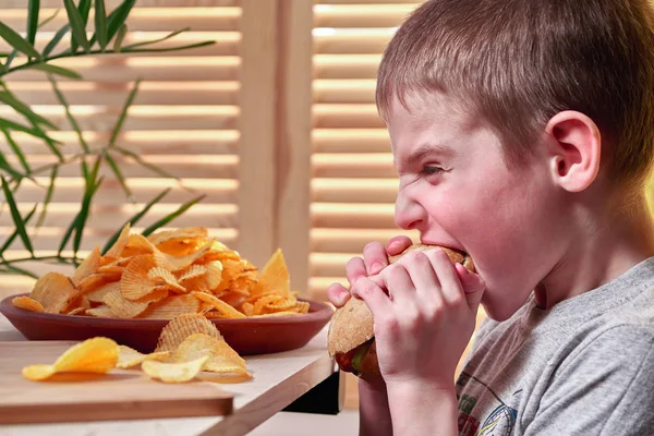 Băiatul mușcă cu nerăbdare delicios hot dog mare. Copilul mănâncă într-un fast food . — Fotografie, imagine de stoc