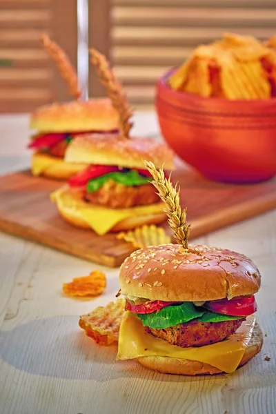 Hamburguesa de comida rápida hecha en casa, con carne, lechuga, tomate, queso, pepinillos y mayonés sobre tabla de madera y mesa. Espacio libre para texto sobre fondo de madera . — Foto de Stock