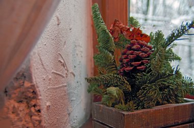 Kavram rahat kış akşam. Natürmort: iğne yapraklı dalları ve çam koni arka planda bir eski beyaz sıvalı duvar ve karla kaplı ağaçlar ile pencere. Çatı tasarım.