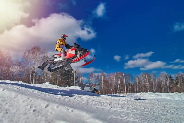 Sports race snowmobiles. Snowmobile in  high jump above track. Sportsman on snowmobile. Winter competition, sunny day, blue sky. Copy space. — Stock Photo, Image