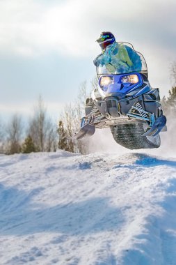Sport blue snowmobile jump. Cloud of snow dust from under snowmobile tracks. Front view, vertical shot. clipart