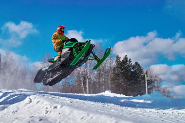 Big green Sport snowmobile jump. Cloud of snow dust from under snowmobile tracks. clipart