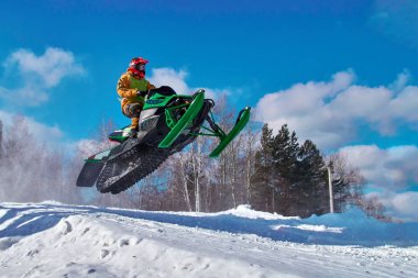 Big green Sport snowmobile jump. Cloud of snow dust from under snowmobile tracks. clipart