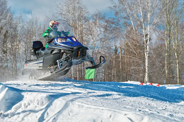Sport blue snowmobile jump. Sunny winter day with blue sky. Concept quick movement.