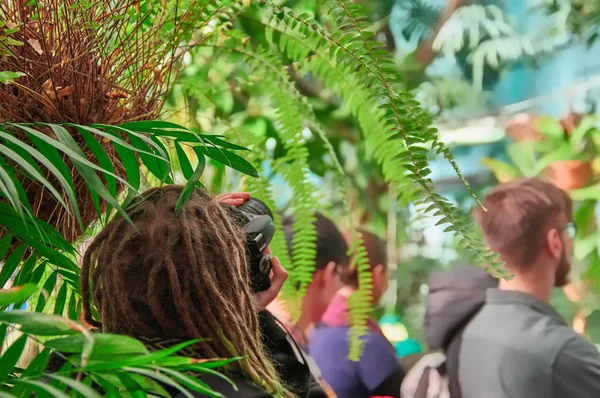 Concetto - fotografia su un'escursione. Fotografo con i dreadlocks sulla sua testa che scatta in giardino botanico tropicale della serra . — Foto Stock