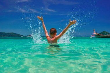 Denizde sıçramasına çocuk. Neşeli çocuk (8-11 yaş arası) su turkuaz denizde elini kaldır. Deniz manzarası, parlak gökyüzü ve deniz. Arkadan Görünüm.