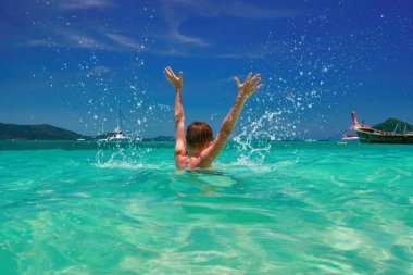 Su sıçramasına çocuk. Neşeli çocuk (12 yaşında) tropikal turkuaz denizde elini kaldır. Deniz manzarası, parlak gökyüzü ve deniz. Arkadan Görünüm.