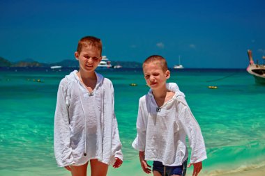 Güneşli tropik sahilde iki erkek kameraya bak. Çocuk beyaz pamuklu gömlek ultraviyole güneşe maruz kalma kendilerini korumak için giyinmiş.