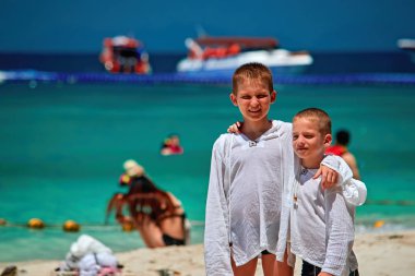 İki küçük kardeş kucaklayan tropikal egzotik Cennet plaj üzerinde durmak. Çocuk beyaz gömlek ultraviyole radyasyon güneşten korunmak için giyindin. Mutlu gülümseyen çocuklar.